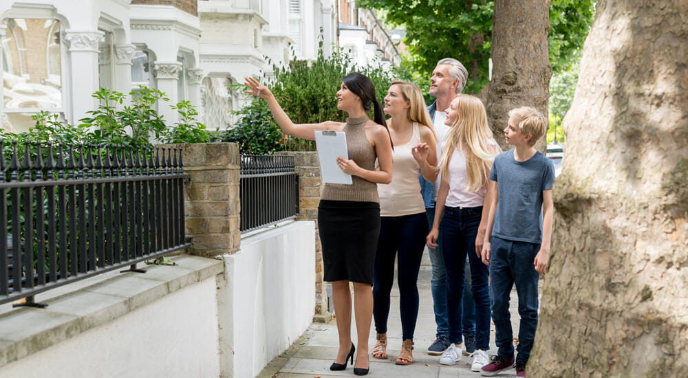Family being show the outside of a house for sale by their real estate agent